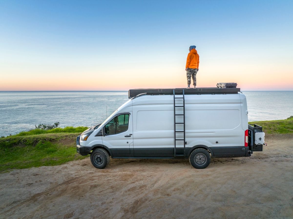 Illustrative sample photo: off-grid-ready high-top panel van conversion with roof rack and ladder, parked on a coastal clifftop. Not the actual vehicle.