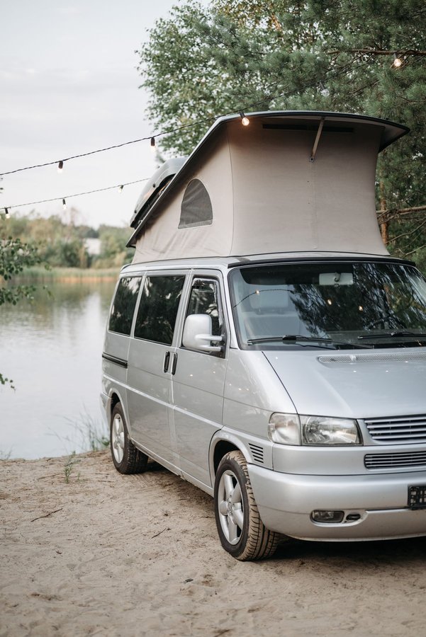 Illustrative sample photo: silver VW-style campervan with pop-top roof raised, parked by a lake. Not the actual vehicle.